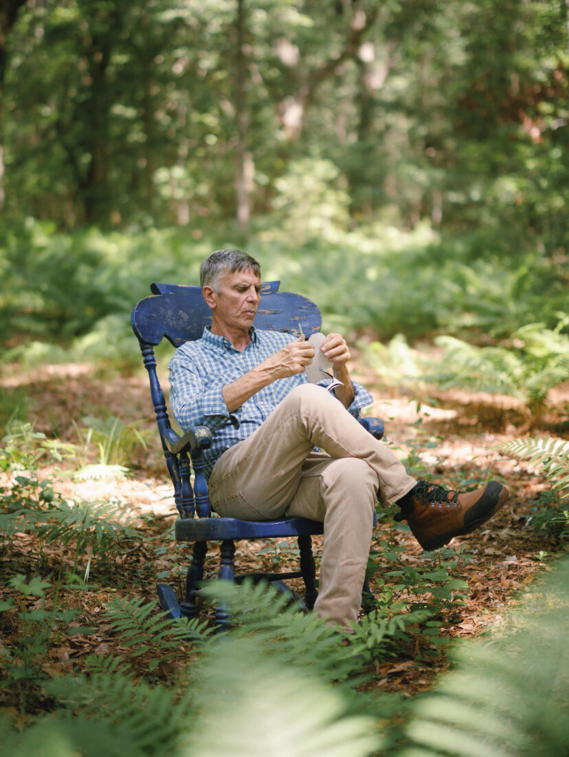 In the woods, a man in a chair cuts a piece of paper