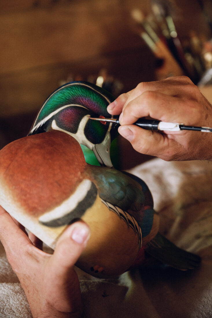 A hand paints a wood duck decoy
