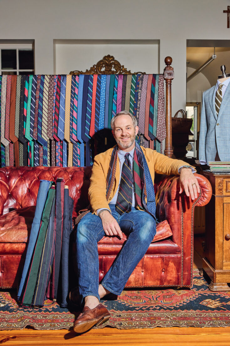 A portrait of a man in a clothing store. He wears ties around his neck
