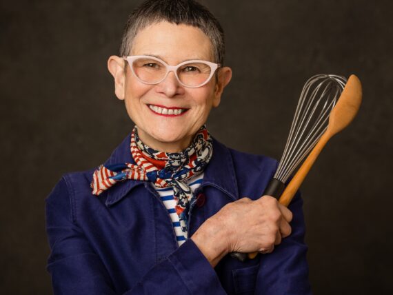 A portrait of a woman holding a whisk and wooden spoon