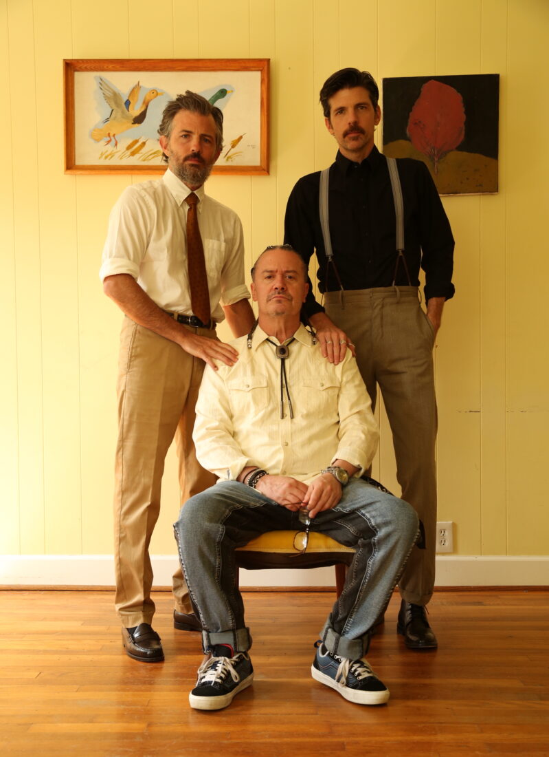 A portrait of three men in a yellow room