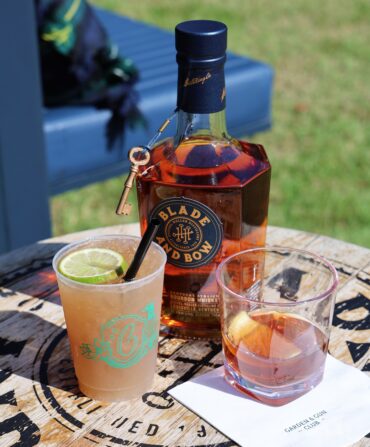 two cocktails on a barrel table with a bottle of Blade and Bow bourbon