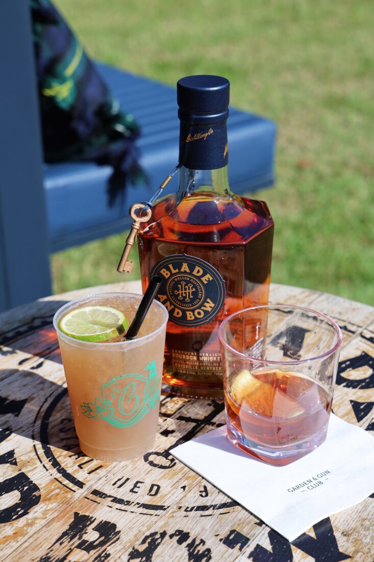 two cocktails on a barrel table with a bottle of Blade and Bow bourbon
