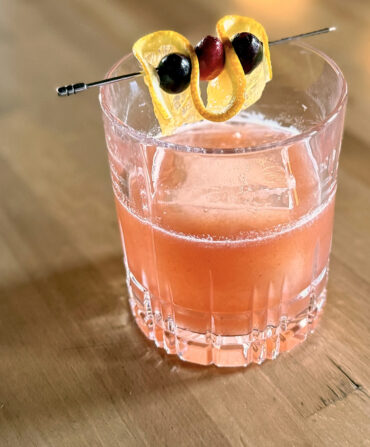 A light pink cocktail with a lemon and cherry garnish