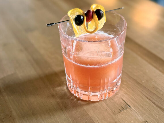 A light pink cocktail with a lemon and cherry garnish