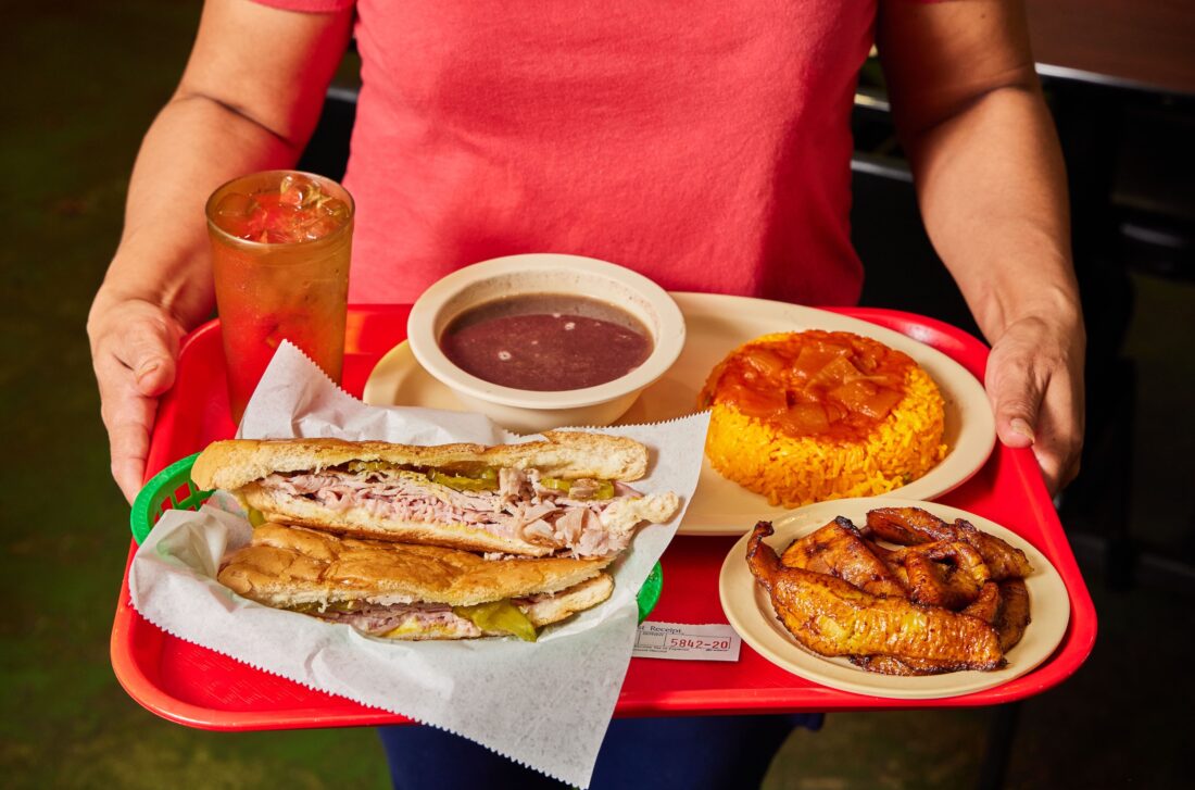 A Cuban sandwich platter with black bean soup, yellow rice, and sweet plantains.