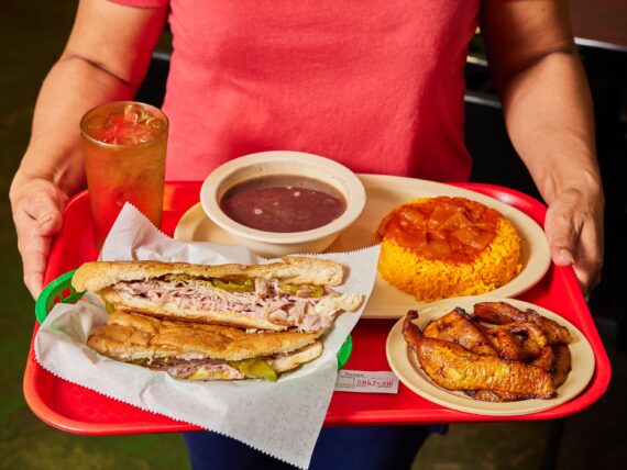 A Cuban sandwich platter with black bean soup, yellow rice, and sweet plantains.