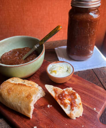 A bowl of jam, a jar of jam, and a baguette smeared with jam