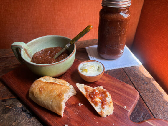 A bowl of jam, a jar of jam, and a baguette smeared with jam