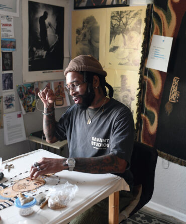 A portrait of an artist sewing beads onto a canvas in a studio