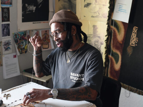 A portrait of an artist sewing beads onto a canvas in a studio