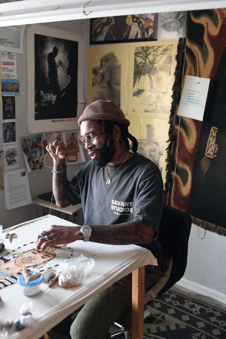 A portrait of an artist sewing beads onto a canvas in a studio