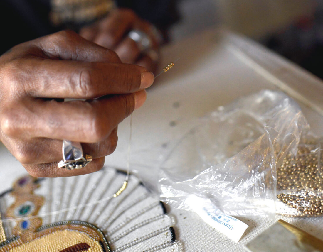 A hand sews beads onto a canvas