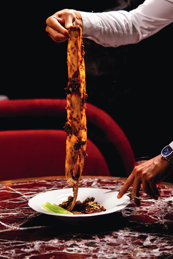 A hand pulls a strand of noodles