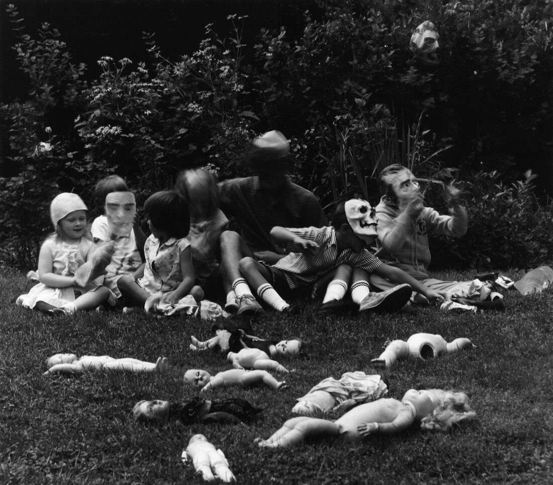 A black and white photo of people with masks in the grass with dolls