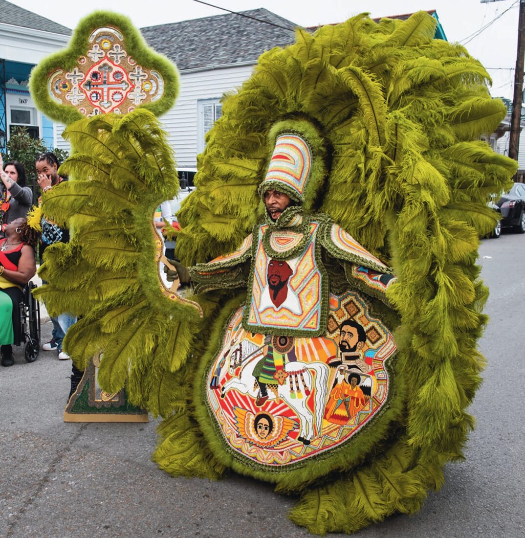 A man wears a large colorful green feathered costume