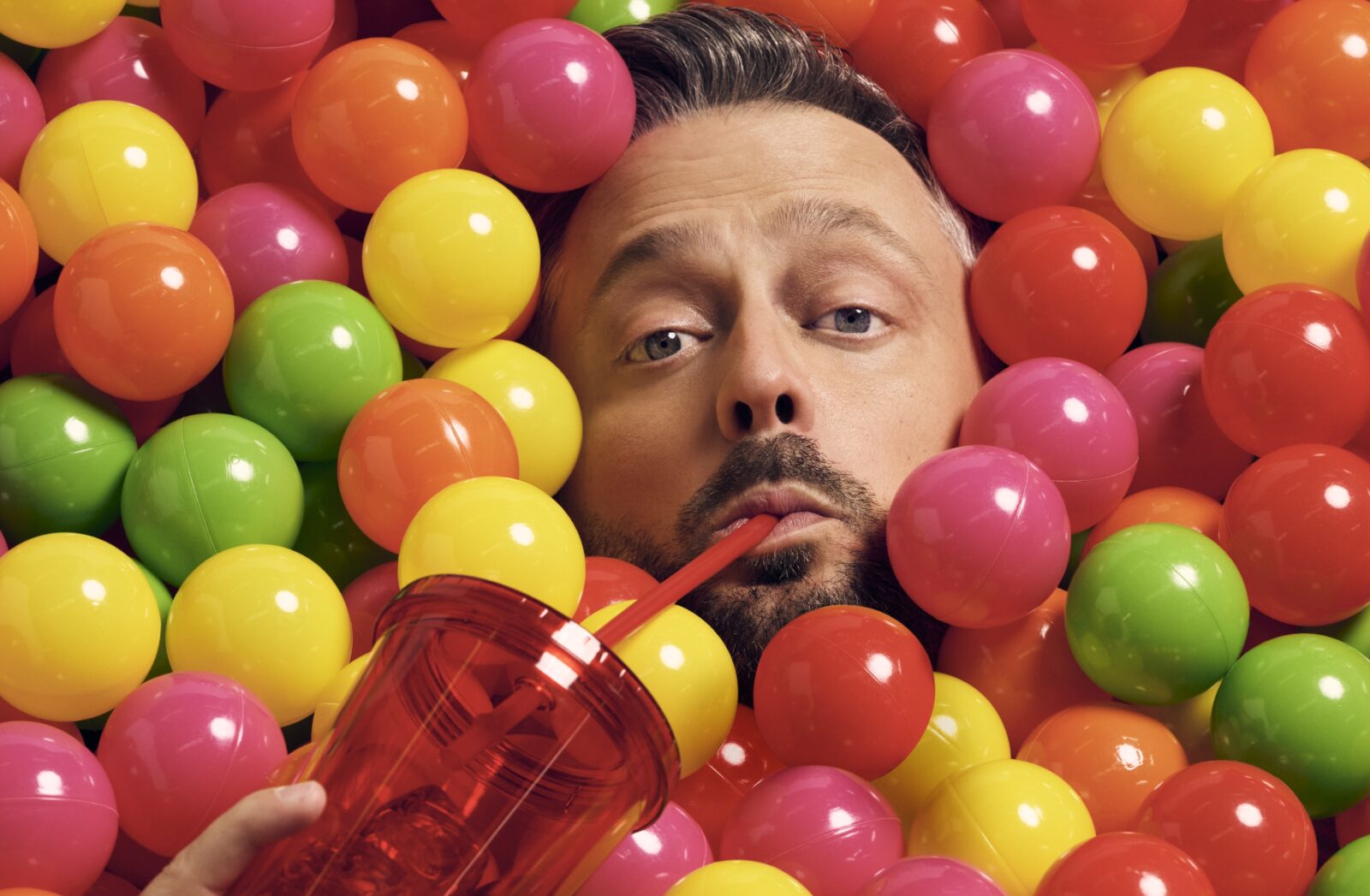 A portrait of Nate Bargartze in a ball pit