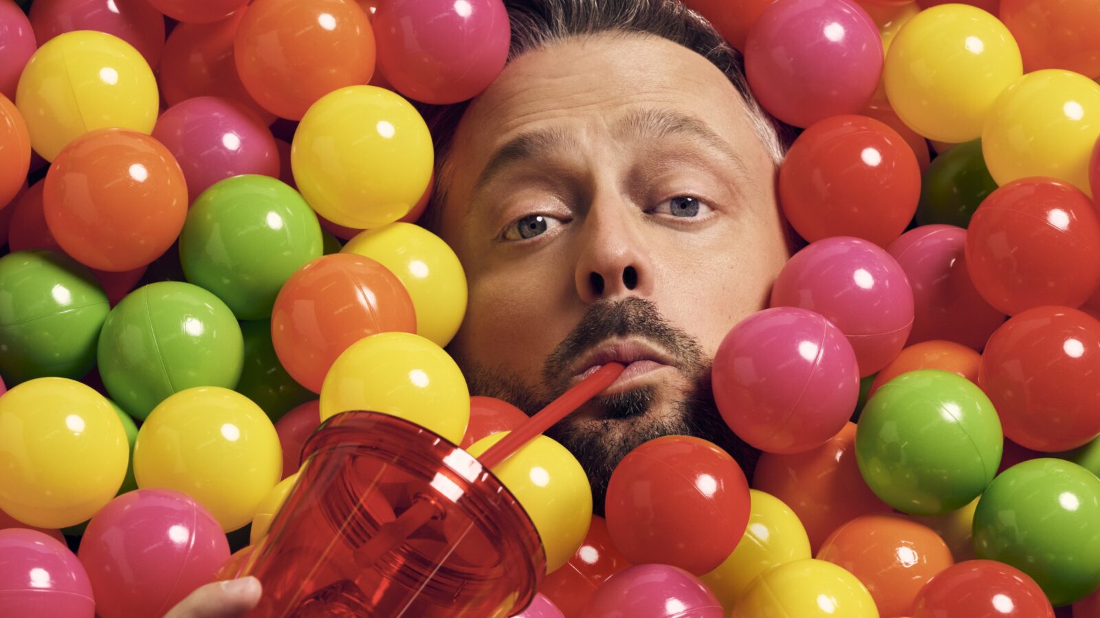 A portrait of Nate Bargartze in a ball pit