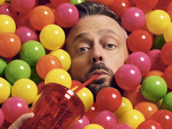 A portrait of Nate Bargartze in a ball pit