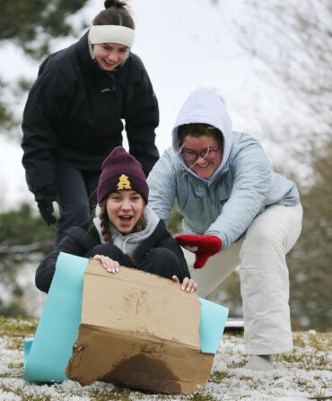 People sled down a snowy hill on a cardboard box