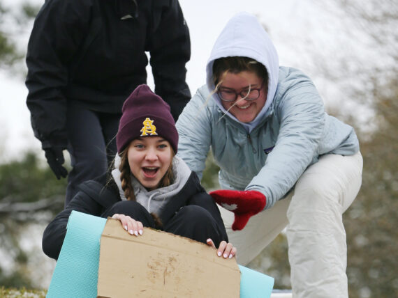 People sled down a snowy hill on a cardboard box