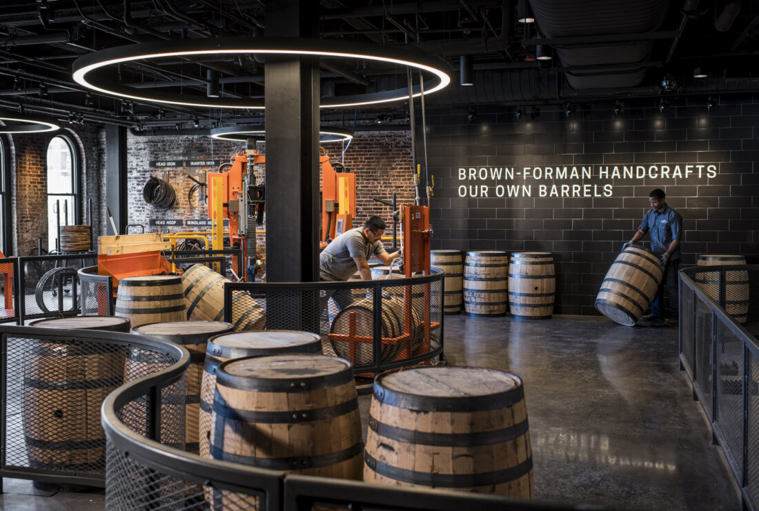 Inside a distillery with people handling bourbon barrels