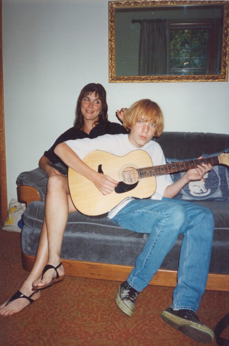 A boy and his mother on a couch; the boy holds a guitar