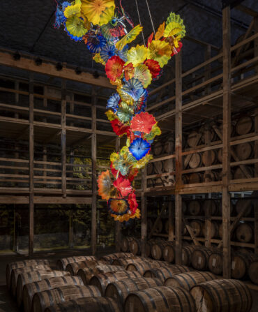 A rainbow glass sculpture hangs above bourbon barrels