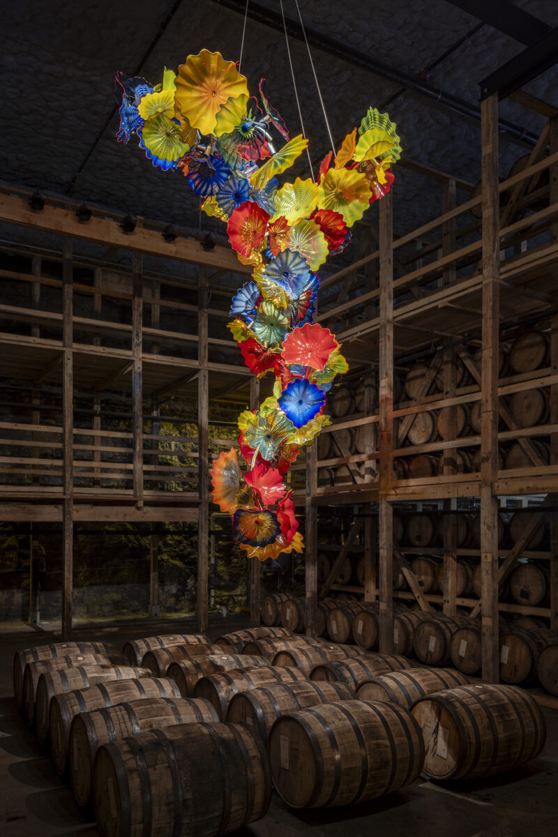 A rainbow glass sculpture hangs above bourbon barrels