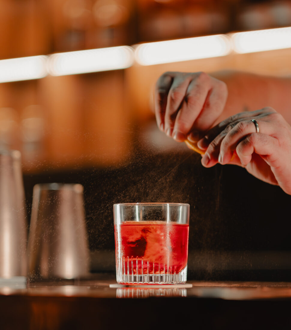 A hand spritzes an orange peel on a drink