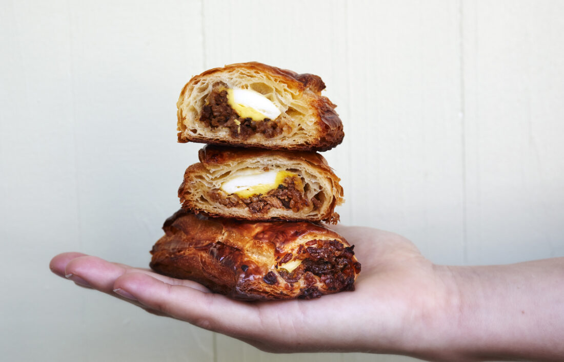 A hand holds a stack of breakfast croissants