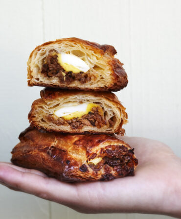 A hand holds a stack of breakfast croissants