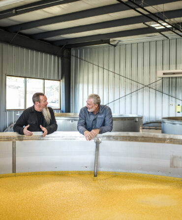 Two men stand over a distilling tank