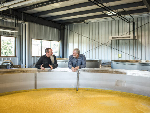 Two men stand over a distilling tank