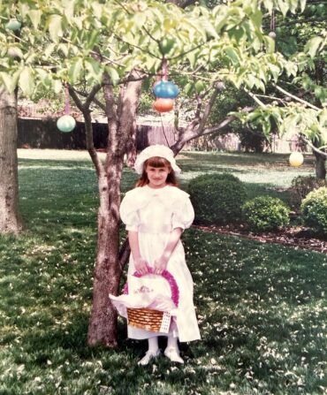A little girl dressed for Easter under a tree with egg decorations