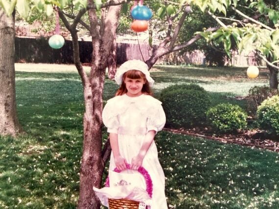A little girl dressed for Easter under a tree with egg decorations