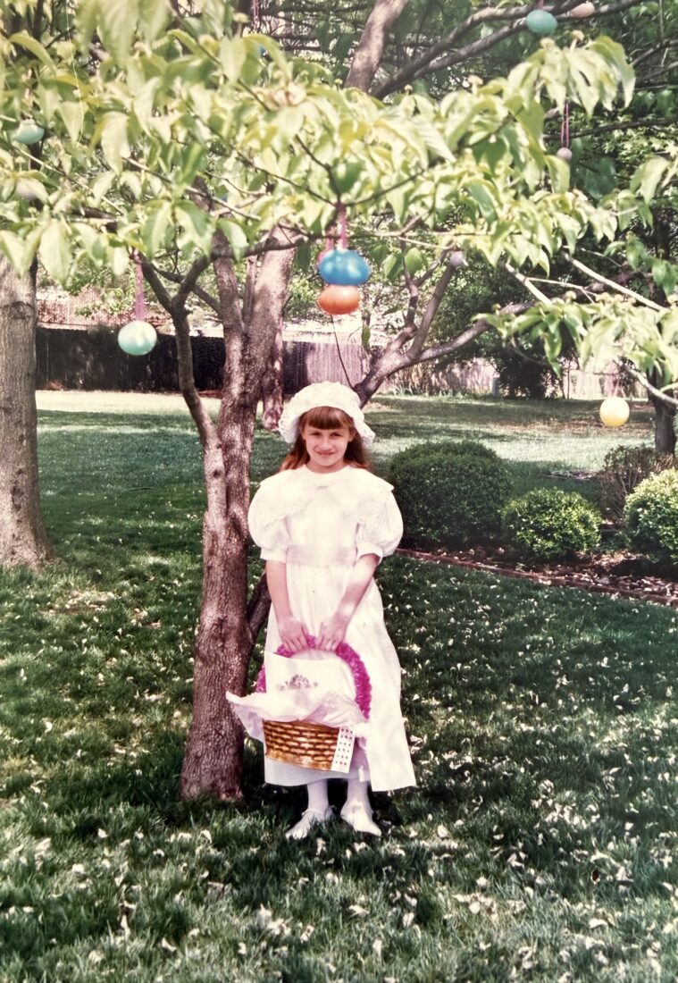 A little girl dressed for Easter under a tree with egg decorations