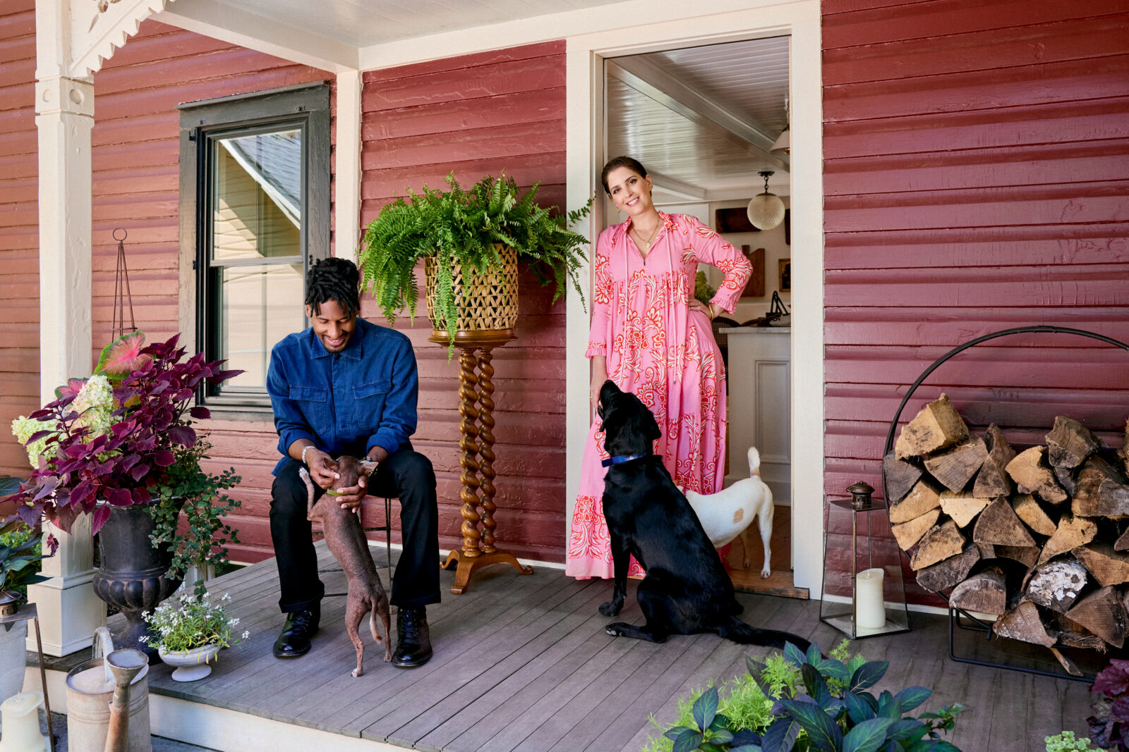 A man, woman, and three dogs on the porch of a red farmhouse