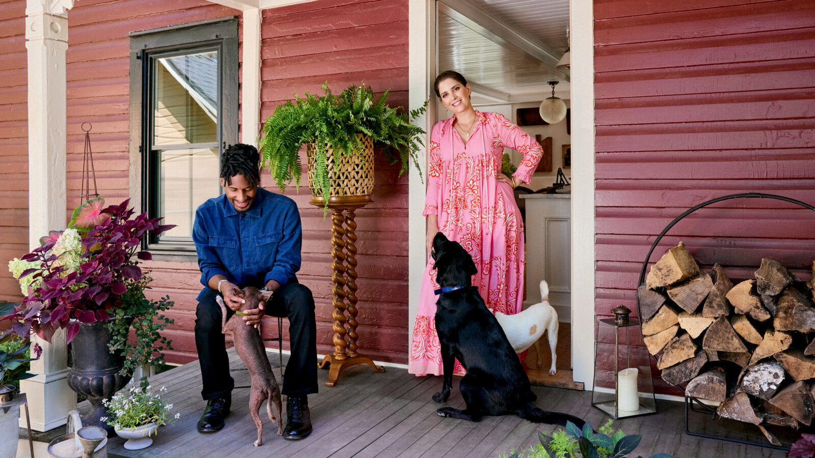 A man, woman, and three dogs on the porch of a red farmhouse