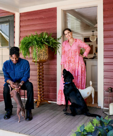 A man, woman, and three dogs on the porch of a red farmhouse