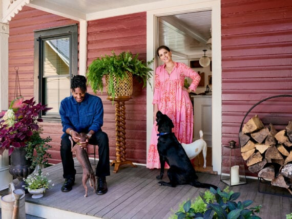 A man, woman, and three dogs on the porch of a red farmhouse