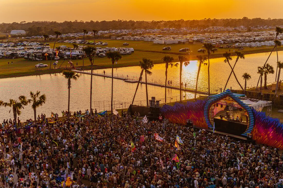 aerial image of a music festival stage and crowd by the water
