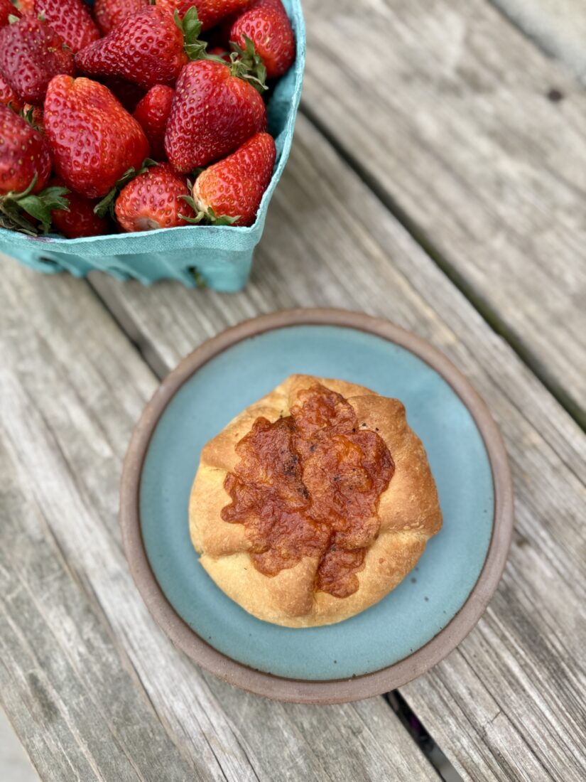 A pastry on a plate next to a basket of strawberries