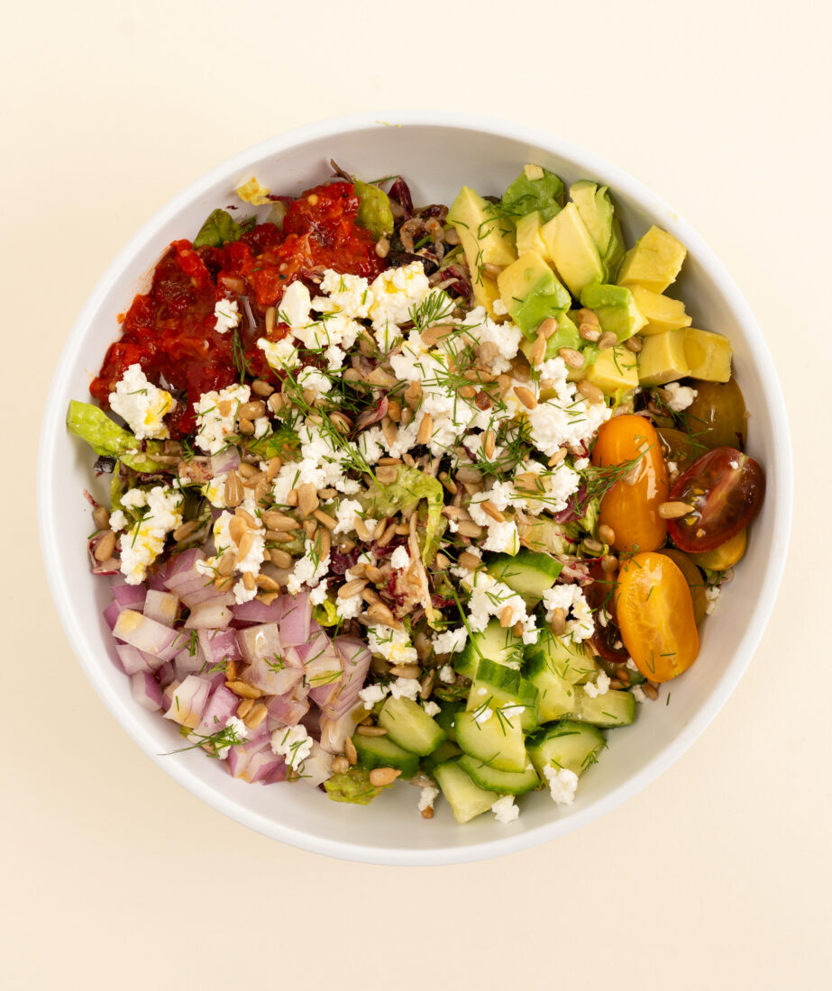 A chopped salad with feta vinaigrette, roasted red pepper, red onion, cucumber, tomato, avocado, and sunflower seeds.