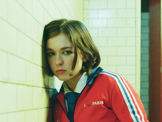A woman in a red jacket leans against a wall