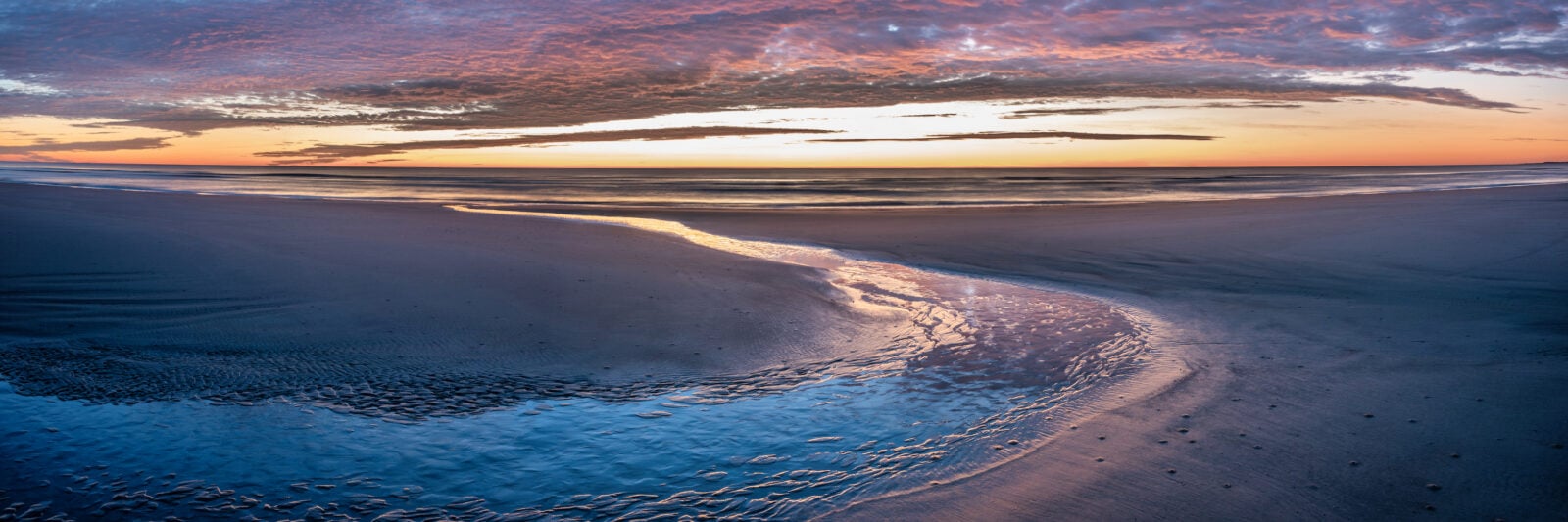 A tide pool empties into the ocean at sunset
