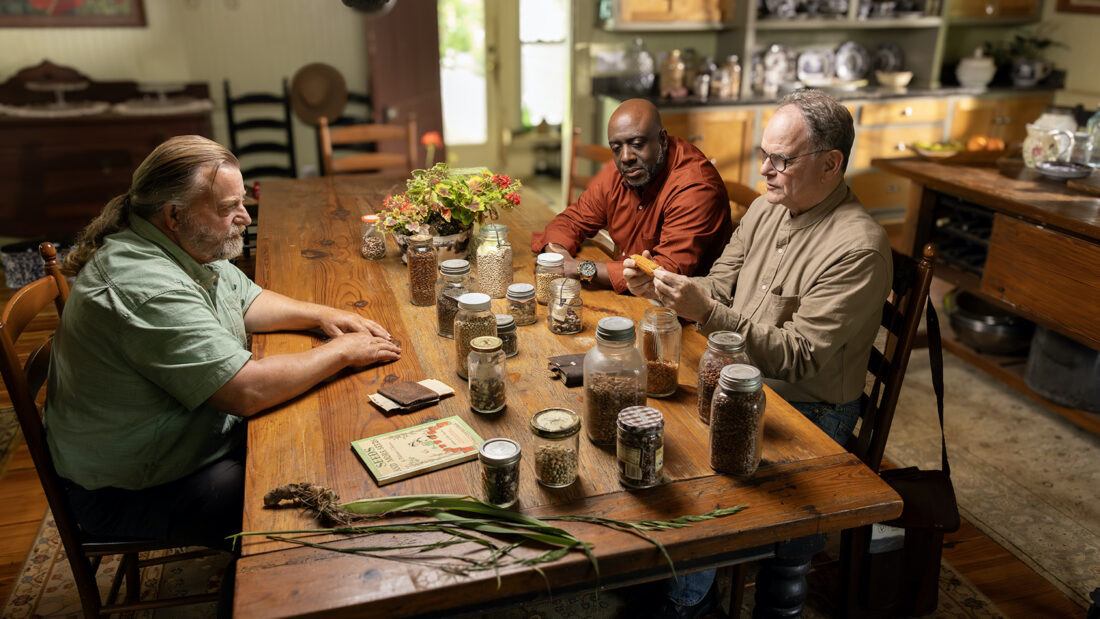 Three men sit at a table with seeds