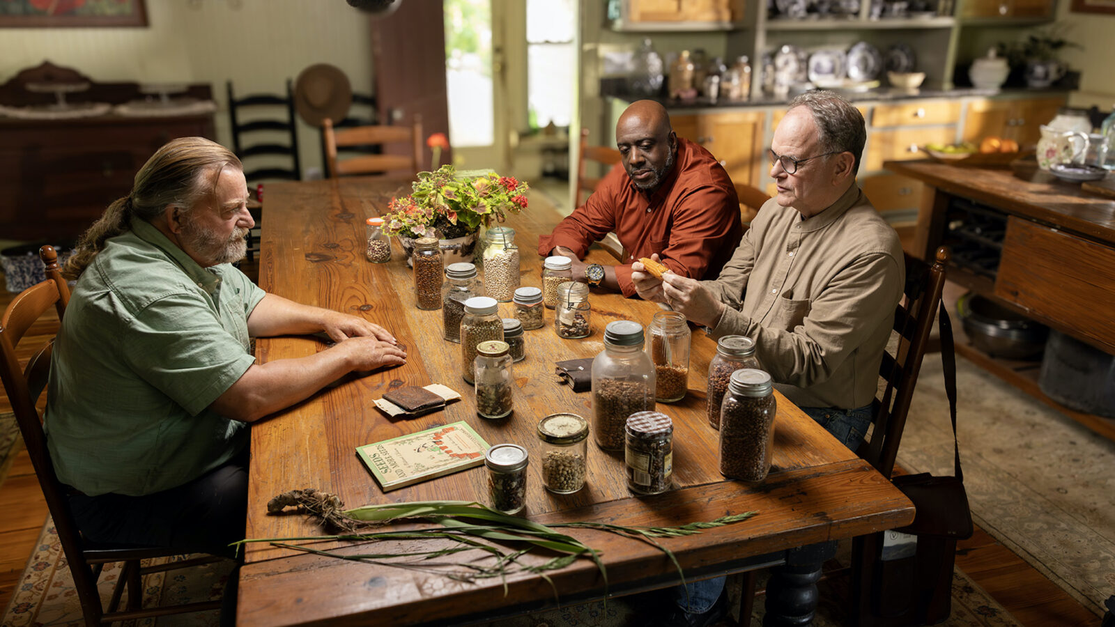 Three men sit at a table with seeds