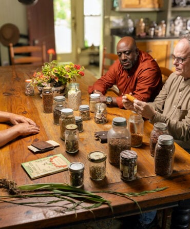 Three men sit at a table with seeds