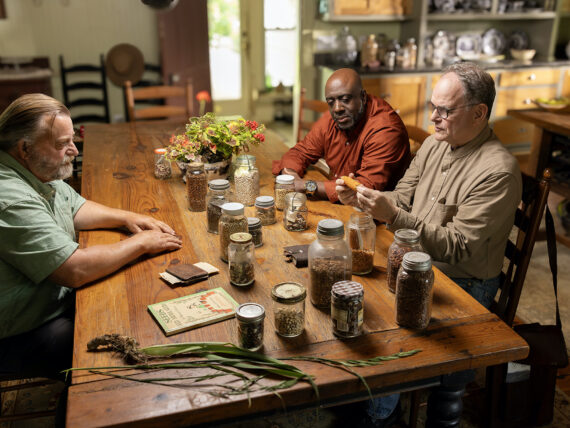 Three men sit at a table with seeds
